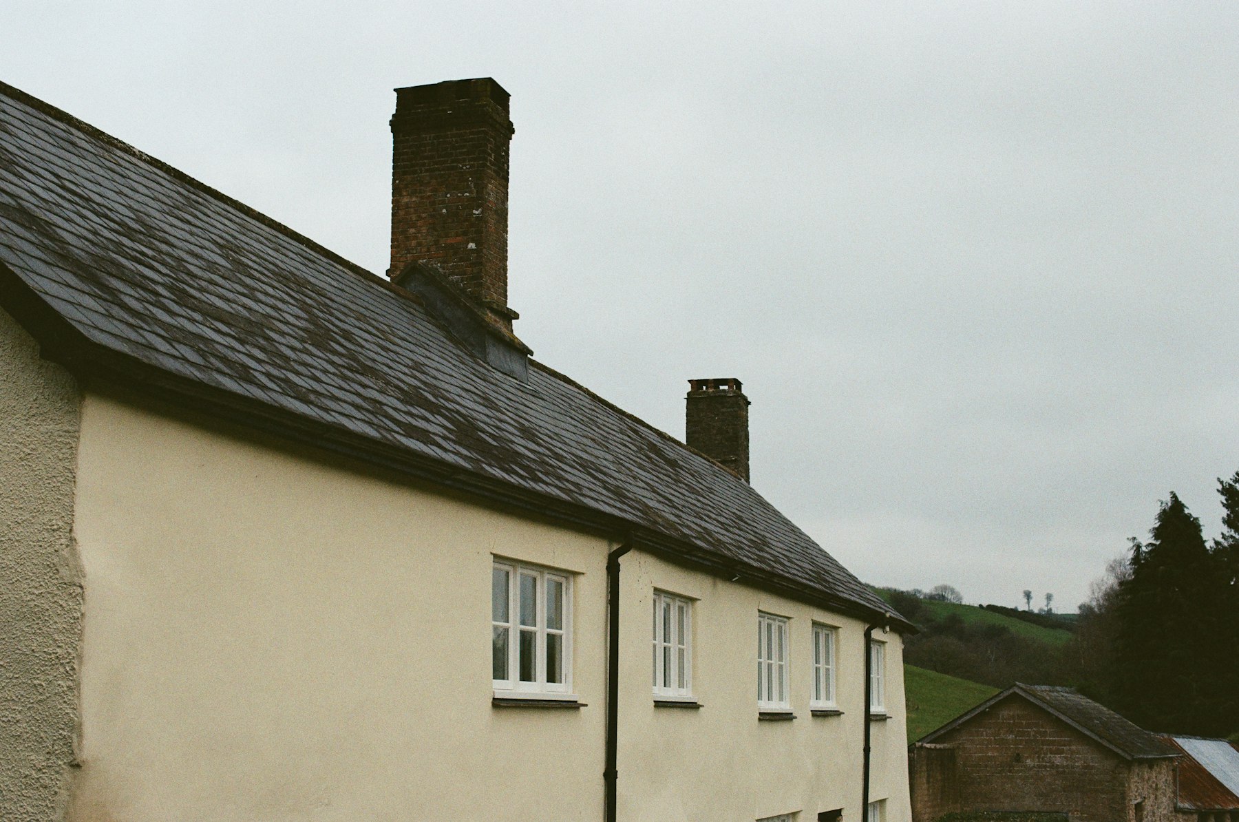 Long Georgia farmhouse with gray slate roof and brick chimneys under overcast sky